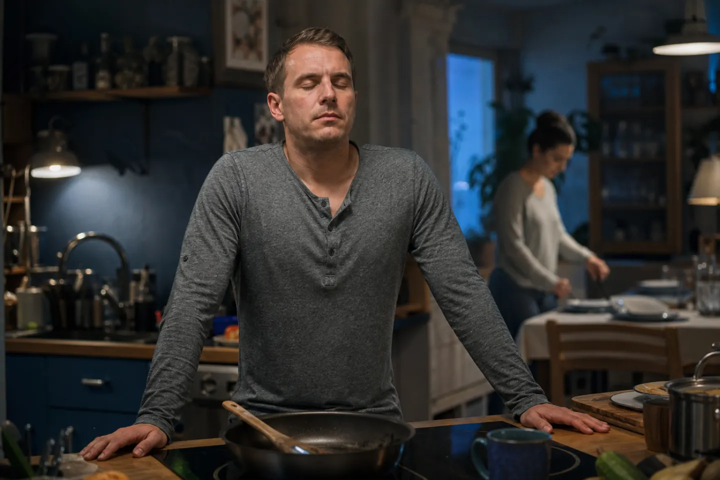 A man pauses with his hands on the kitchen counter, eyes closed, taking a breath before reacting