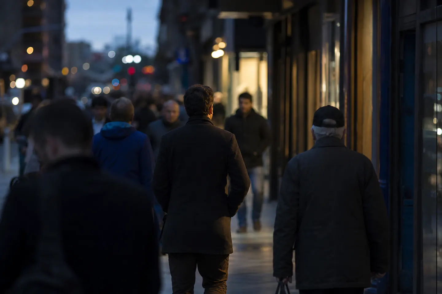 Men of different ages walk along a busy city street at dusk, seen from a distance