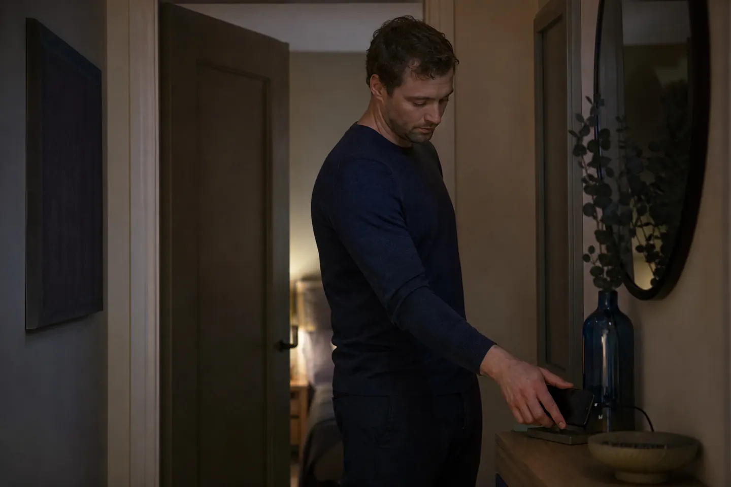 A man leaves his phone charging on a hallway shelf outside the bedroom in the evening